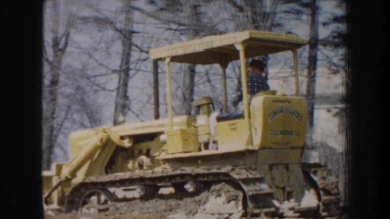 Operator drives a yellow tracked bulldozer in a wooded area.