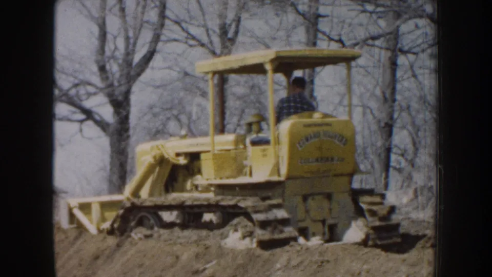 1959 Nebraska frame showing a rear-side view of a yellow tracked bulldozer with the operator seated beneath an open canopy.