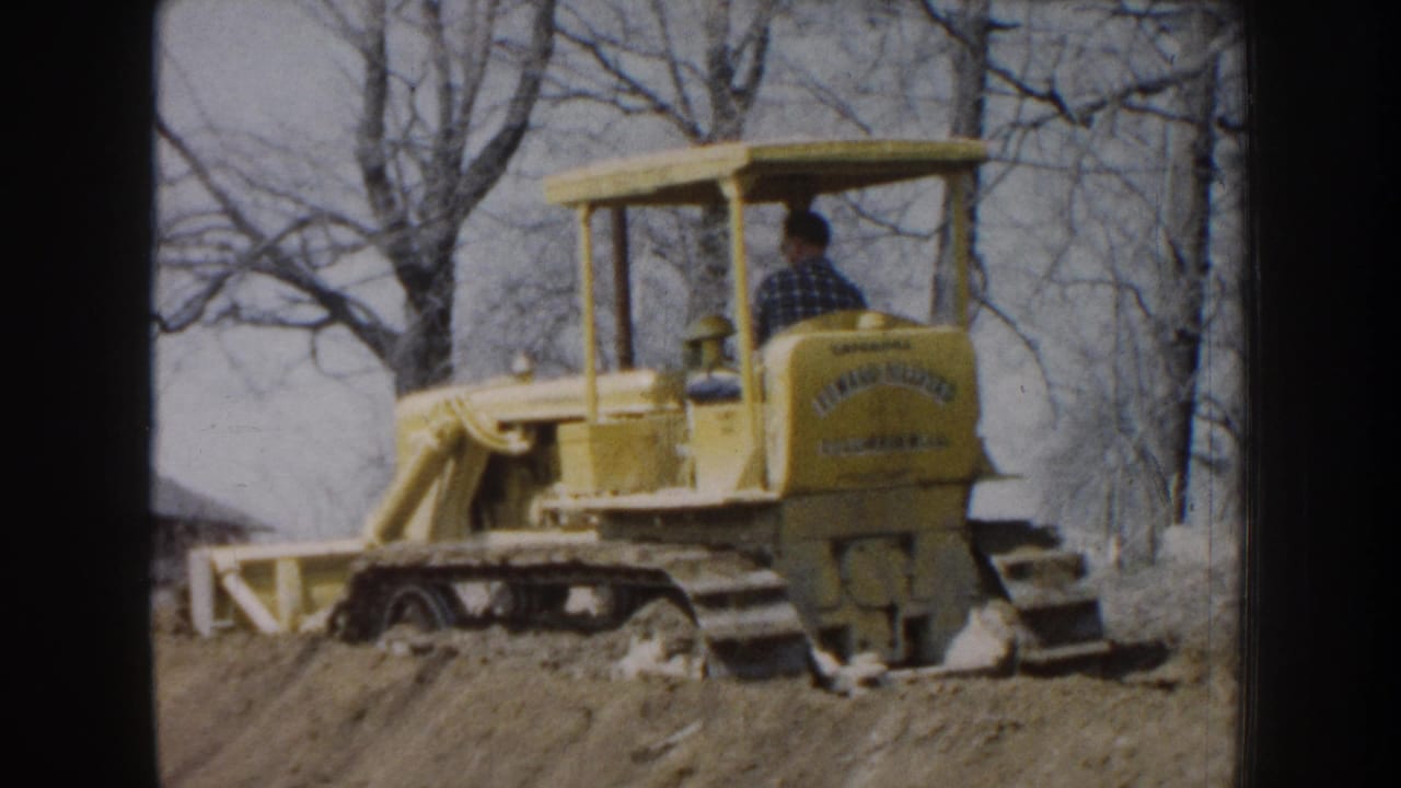 Yellow tracked bulldozer with a seated operator working near bare trees and dirt.
