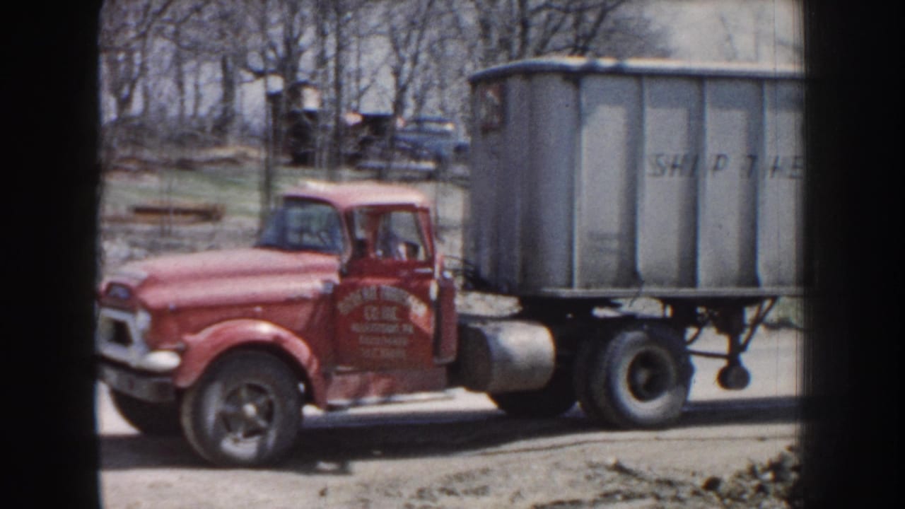 Red truck cab beside a gray trailer with partial lettering, seen through film frame edges.