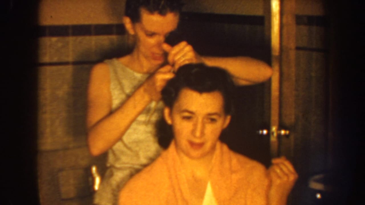 Standing woman works on the seated woman's hair as the seated woman faces forward.
