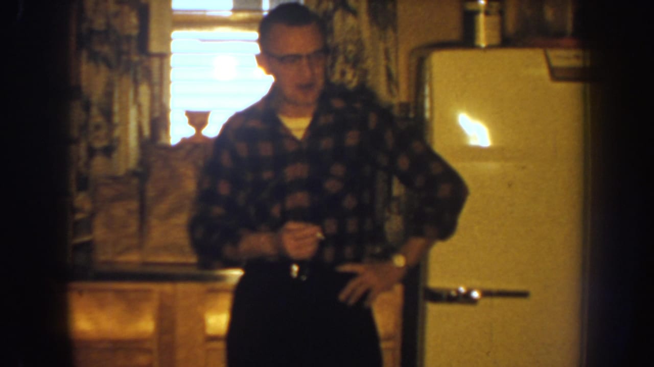 Man holding a small object while standing near a refrigerator and window.
