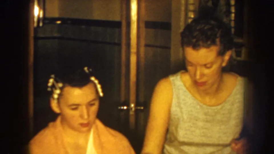 Nebraska 1959 frame of a seated woman with hair rollers beside the woman assisting her in a private room.