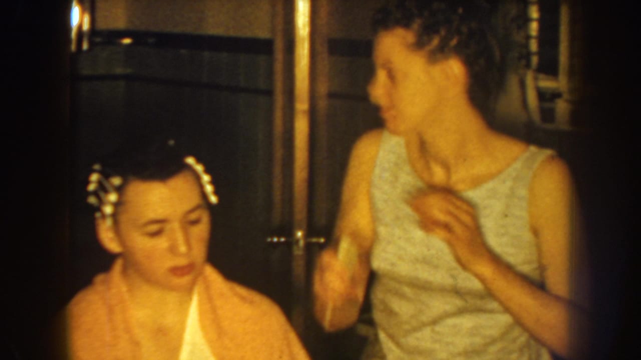In a 1959 Nebraska home-movie frame, a woman stands beside a seated woman whose hair is partly set with curlers.