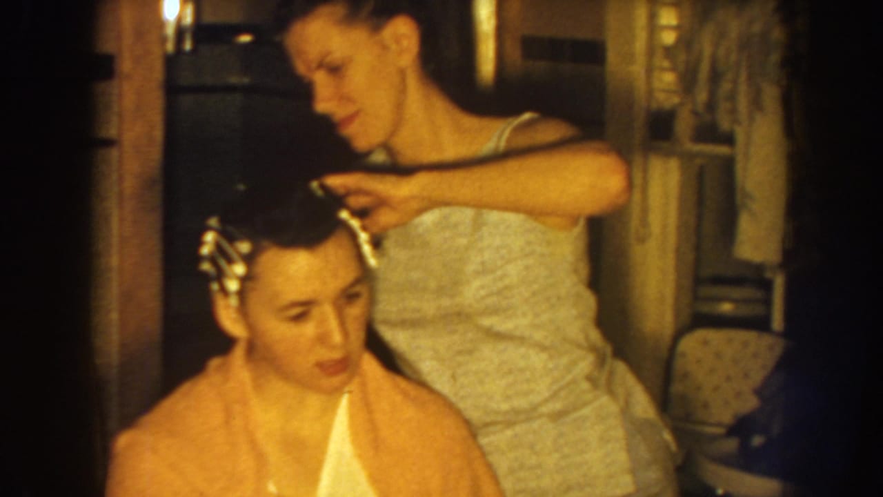Standing woman places curlers into the seated woman's dark hair.
