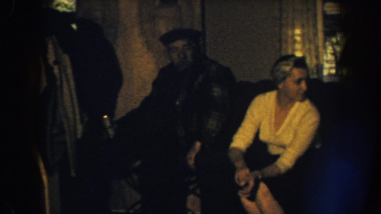A woman in a light sweater turns on a sofa beside a man in a dark cap.
