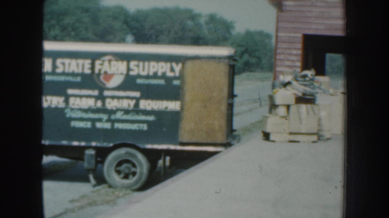 Farm supply truck beside an open doorway with stacked goods near the building.