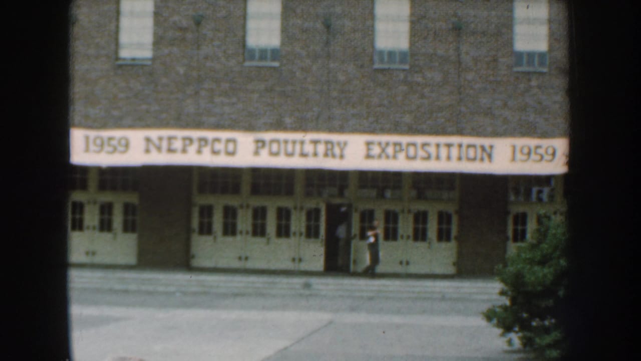 1959 Nebraska exterior view of a brick building with a long NEPPCO Poultry Exposition banner and a person near the entrance.