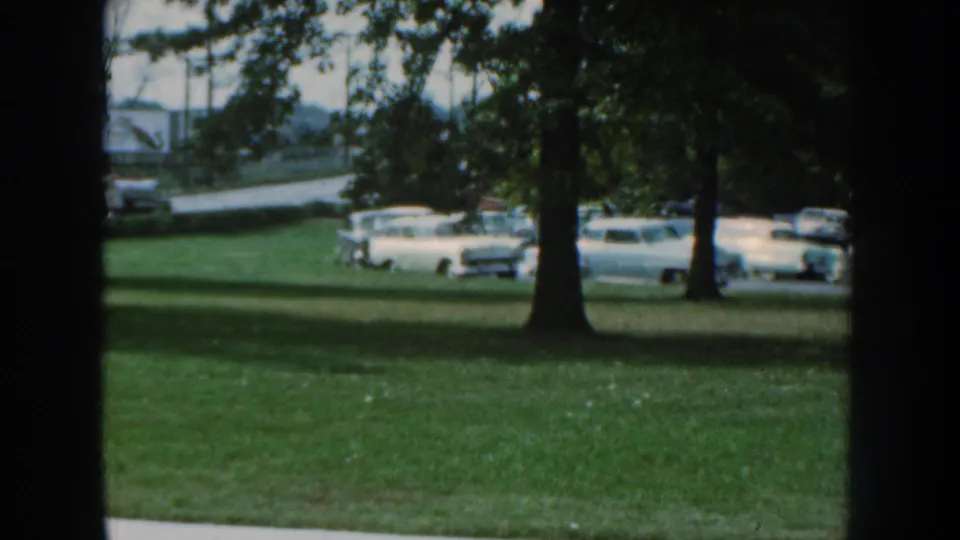 1959 Nebraska outdoor view of parked midcentury cars beyond a lawn and trees near the exposition area.