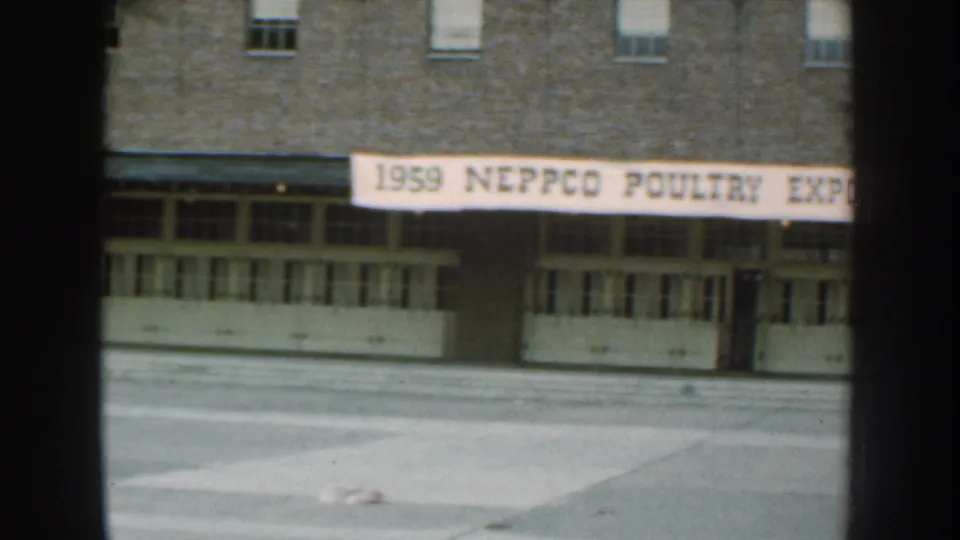 1959 Nebraska frame showing a brick facade with a 1959 NEPPCO Poultry Exposition banner above rows of doors.