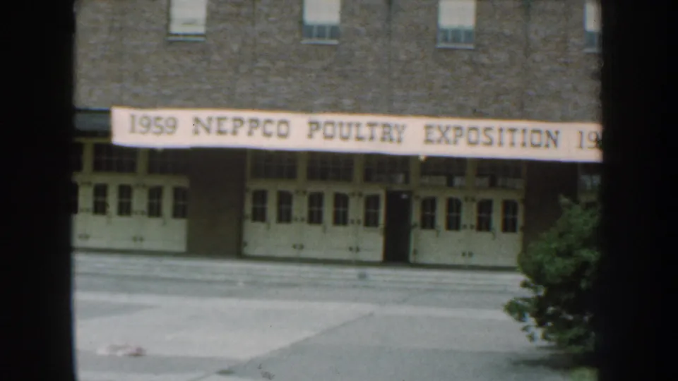 1959 Nebraska home-movie frame showing a brick building facade with a NEPPCO Poultry Exposition banner above white double doors.