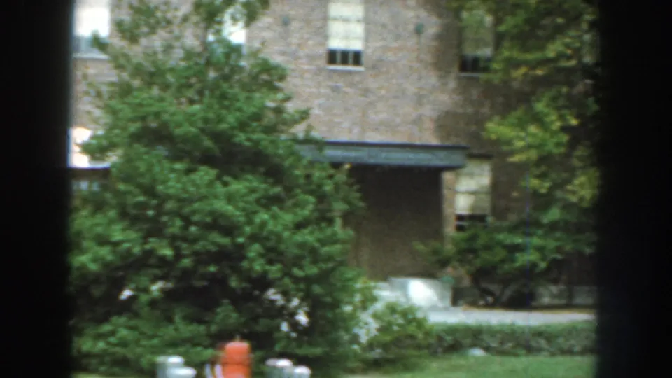 1959 Nebraska home-movie view of landscaped grounds beside the exposition building, with trees, lawn, and a red fire hydrant.