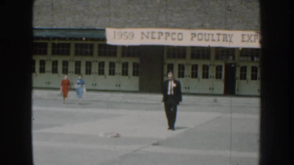 The man continues across the Nebraska expo grounds while two women walk behind him under the 1959 poultry expo banner.