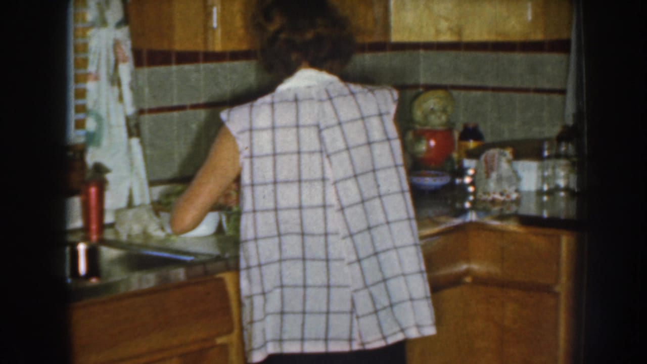 Woman at kitchen counter with wood cabinets and containers behind her.