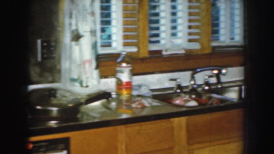 1959 Nebraska home kitchen detail showing the sink, counter items, pan, window blinds, and wood lower cabinets.