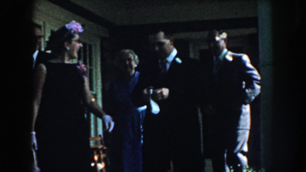 Several formally dressed adults stand in a dark interior near a doorway.