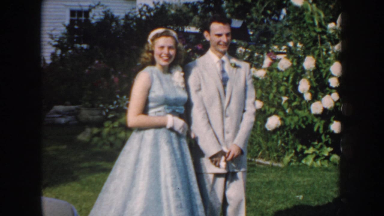 Teenage couple in 1950s formal attire smiles toward the camera in a Nebraska garden setting.