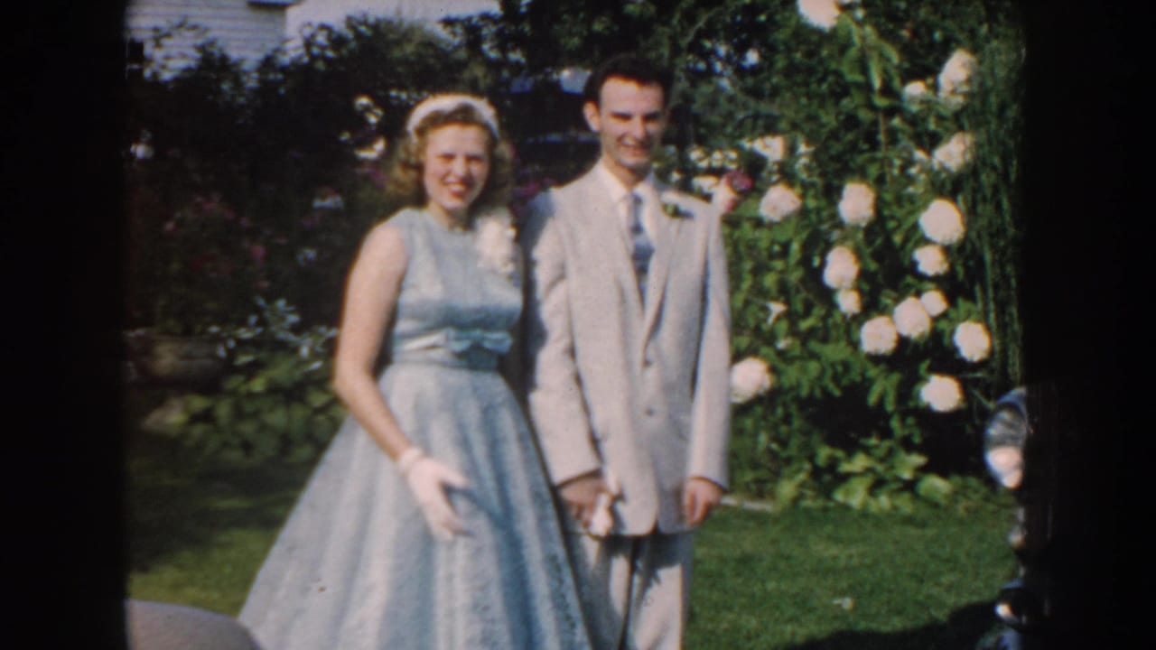 Couple standing close together in a garden with pale flowers behind them.