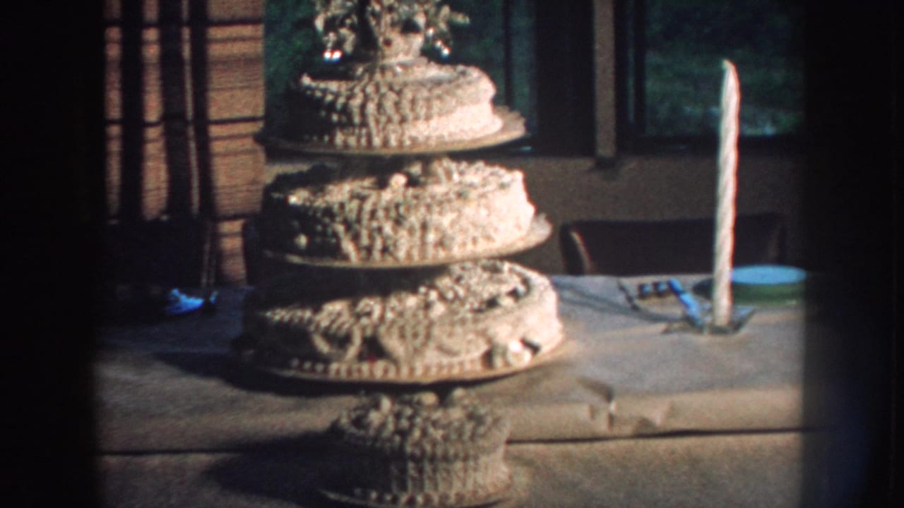 1959 Nebraska 8mm frame showing an ornate multi-tiered wedding cake on a table with a tall candle nearby.