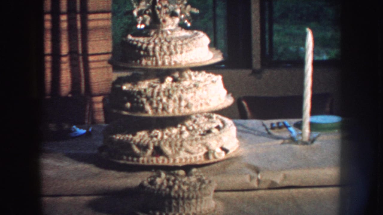 Tiered wedding cake and tall candle on a table near a window.
