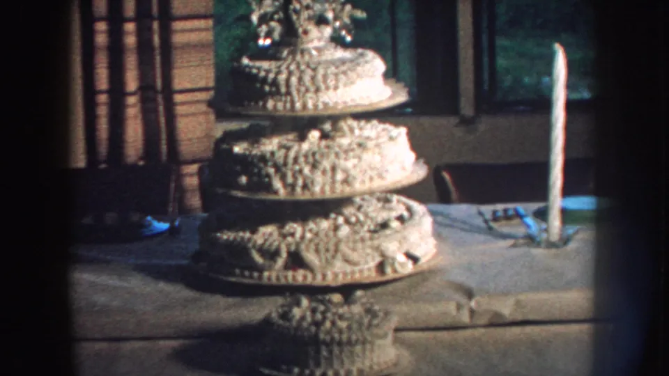 1959 Nebraska 8mm frame showing the wedding cake from a steady home-movie angle with candle and curtains behind.