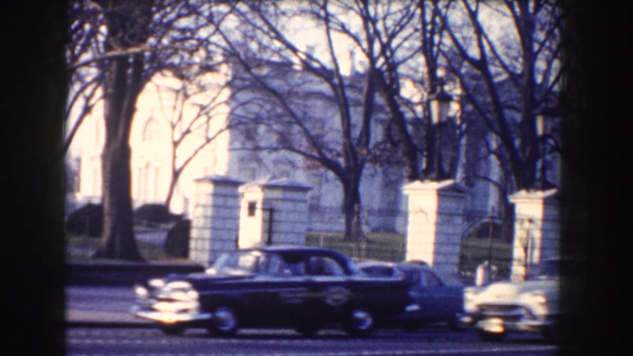 Dark sedan passing the White House behind bare winter trees.