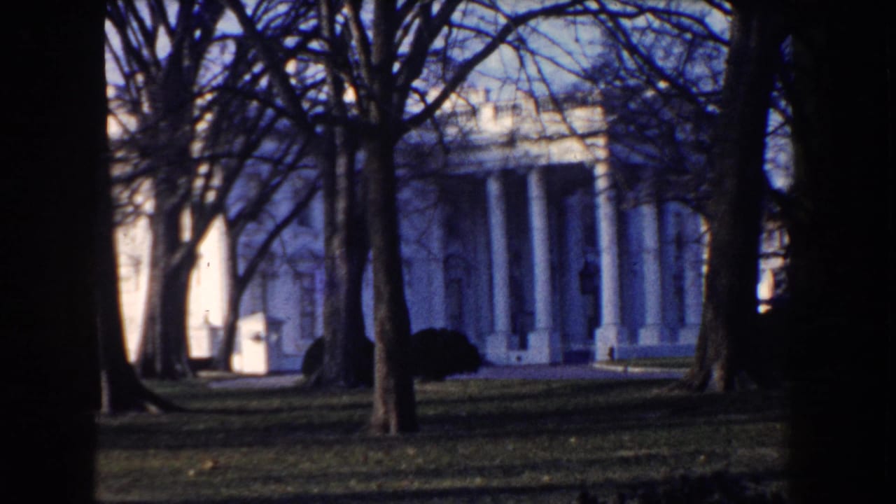 1960 Washington DC home-movie view of White House columns partly obscured by winter trees and a dark film edge.