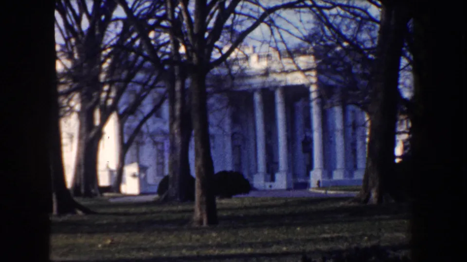 1960 Washington DC home-movie view of White House columns partly obscured by winter trees and a dark film edge.