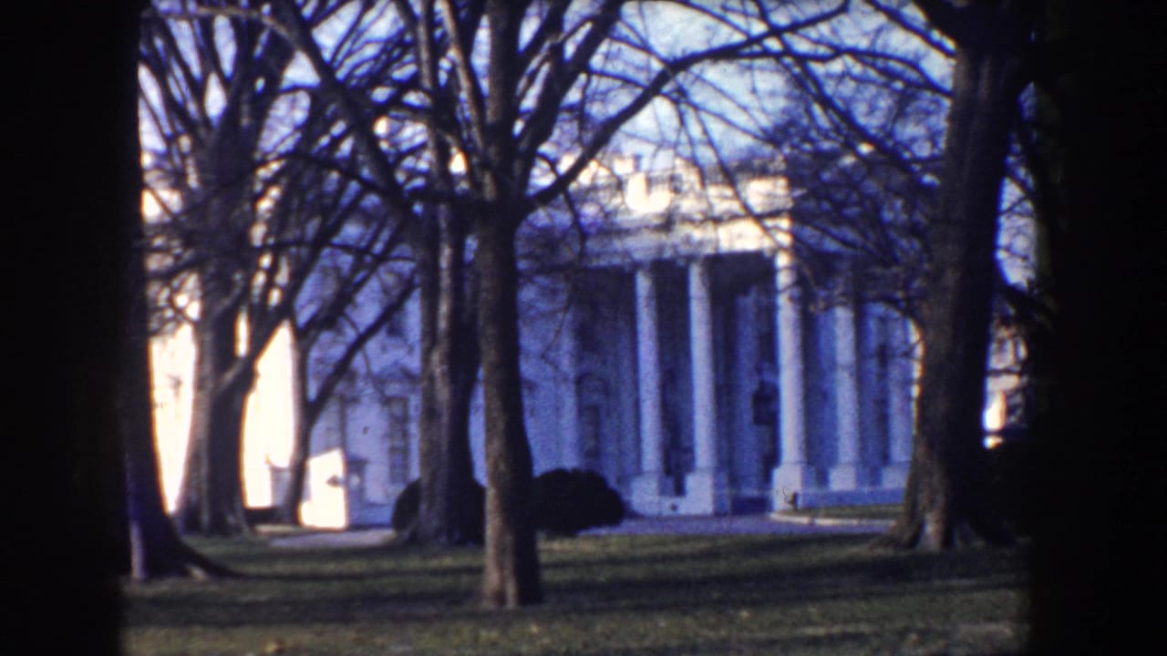 1960 Washington DC frame of the White House seen through bare trees, with lawn and dark vignette around the home-movie frame.