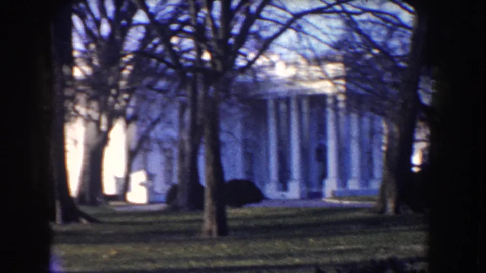 White House exterior in Washington, D.C., framed by bare winter trees in vintage 8mm footage.