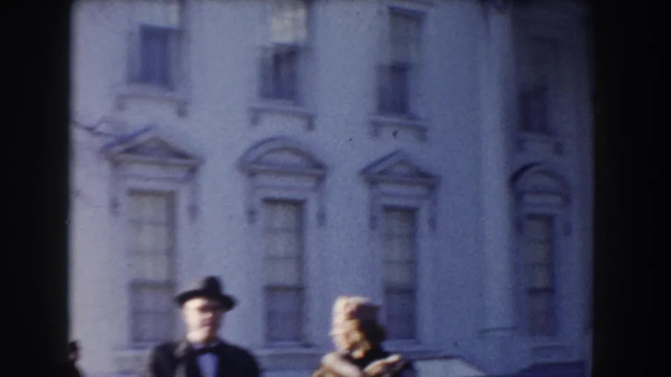 In Washington, DC home-movie footage, a formally dressed man and woman stand near a white civic building facade.