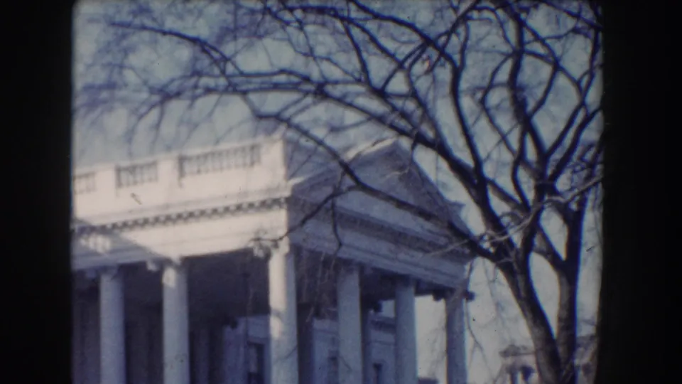 The handheld 8mm view shows a neoclassical Washington, DC facade partly crossed by winter-bare tree branches.
