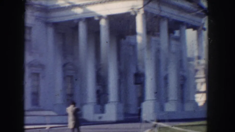 1960 Washington, DC home-movie view of a grand classical facade with tall white columns and a distant pedestrian on the grounds.