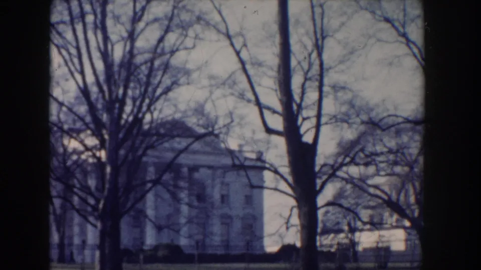 A grand white civic building in Washington, DC appears through winter trees and an iron fence in this 1960 home-movie frame.