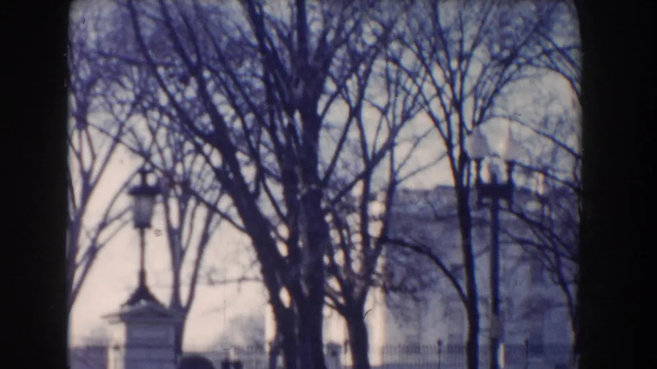 A Washington, DC streetscape with bare trees, lampposts, fencing, and part of a white civic building in a 1960 8mm frame.
