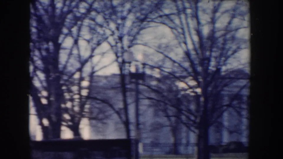 Soft 8mm view of bare trees and a large pale building in Washington DC, partly obscured by dark film edges and tree trunks.