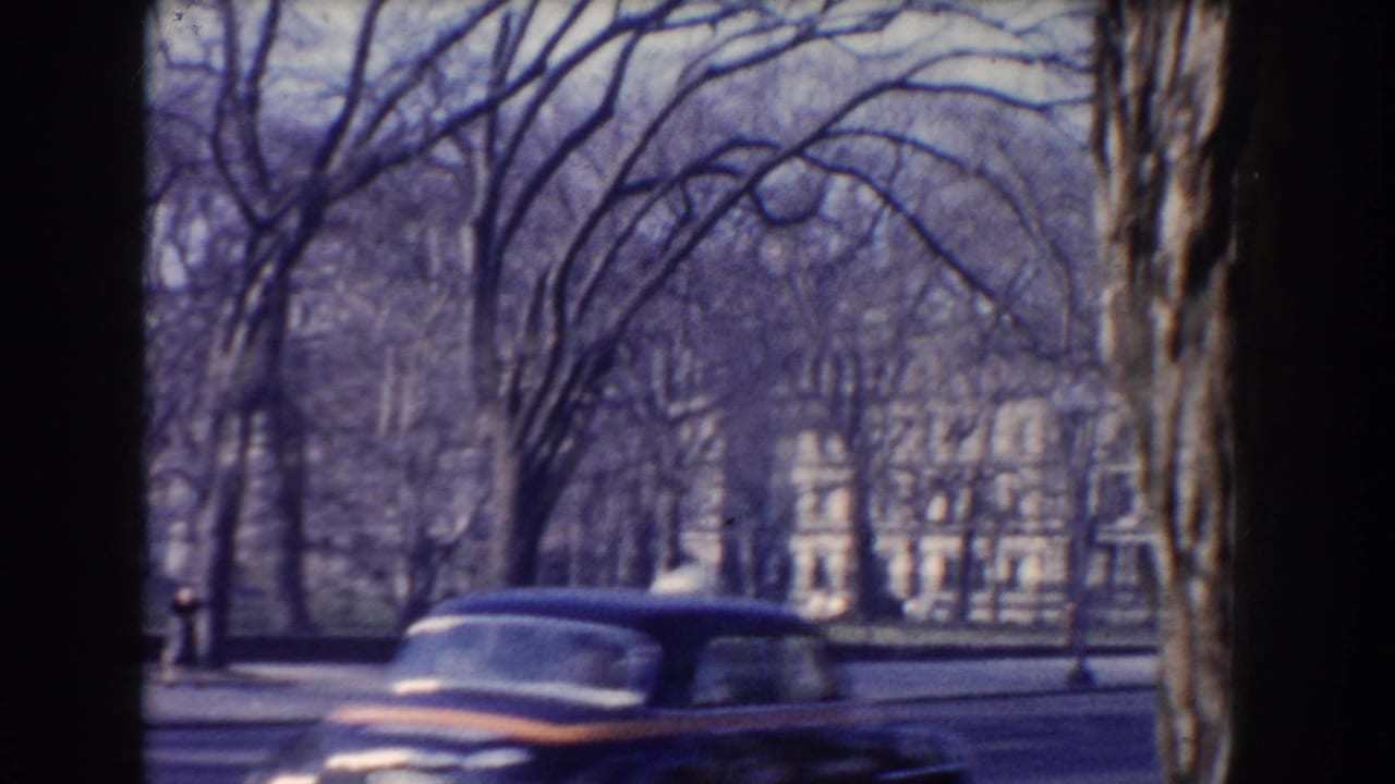A 1960 Washington DC street view shows a dark American car moving past leafless trees with a large white building in the background.