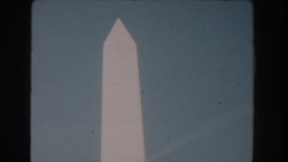 1960s 8mm Washington, DC frame showing the Washington Monument's pointed top centered against a clear blue sky.