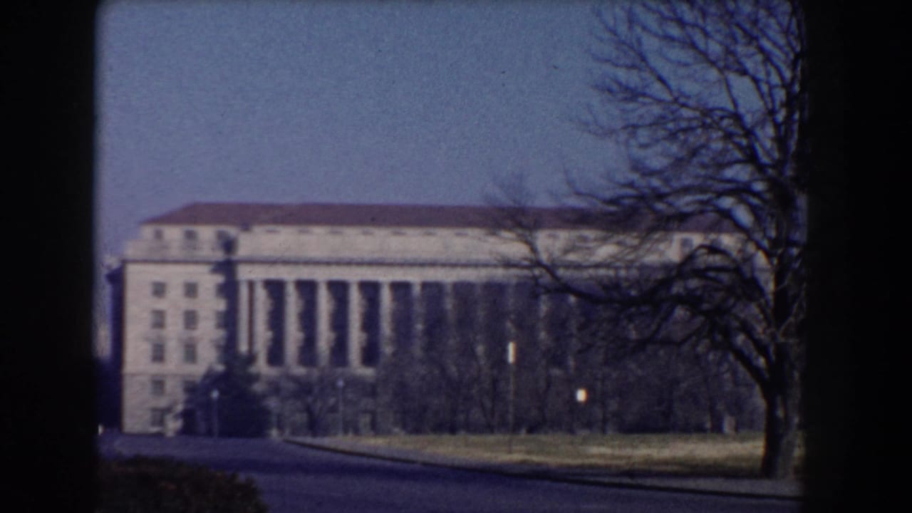 Large columned building seen across a road with bare trees in front.