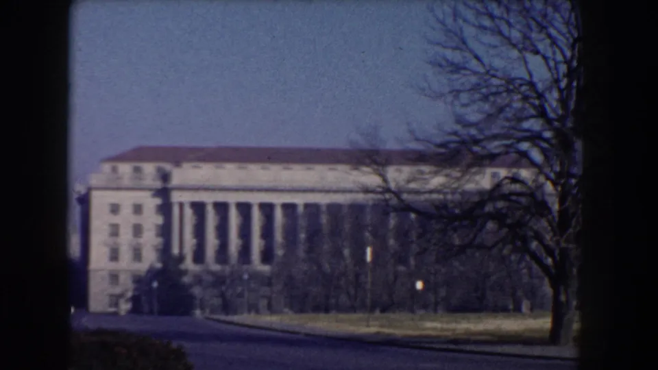Large classical building in Washington, DC, with tall columns, bare trees, lawn, and roadway in a 1960 8mm frame.