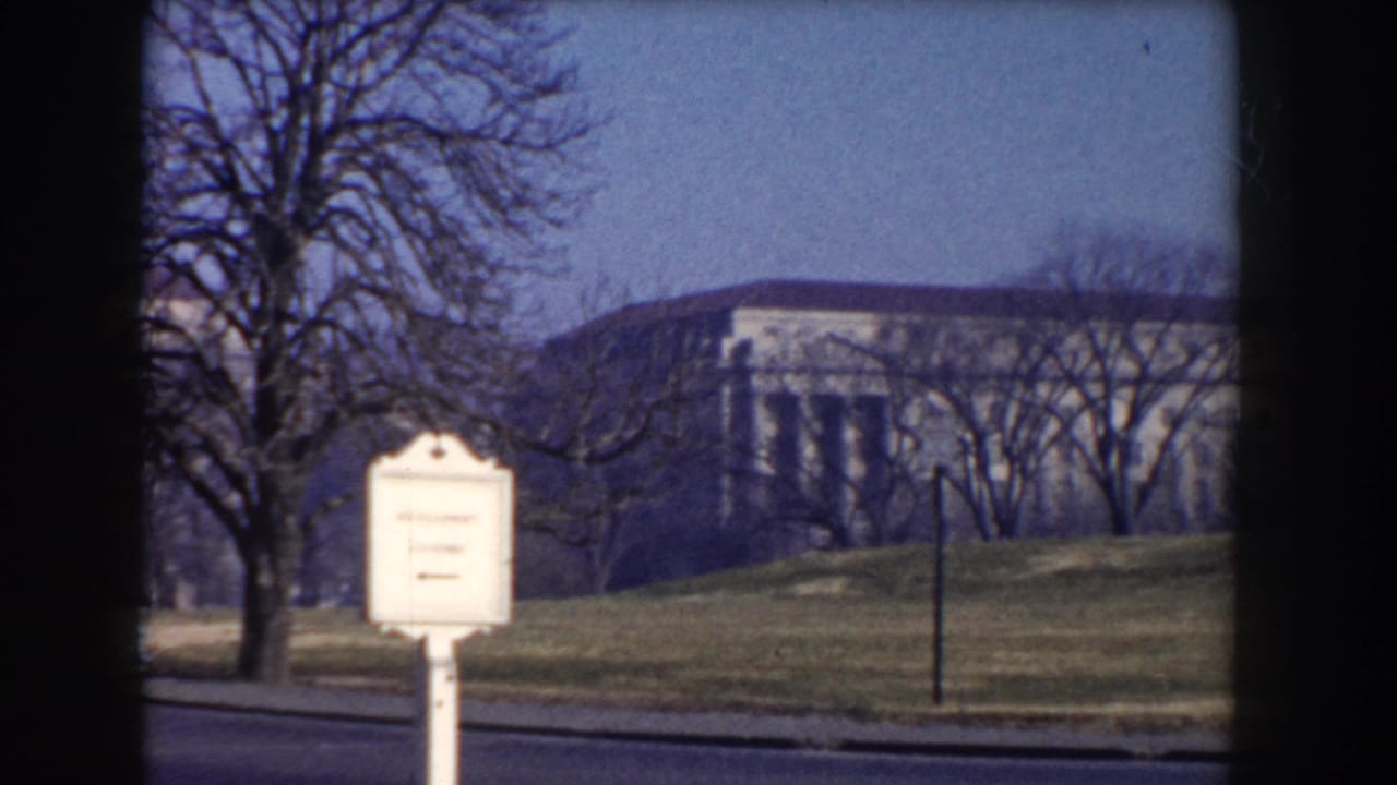 Street edge near the Washington Monument grounds with bare trees, a sign, and a distant building.