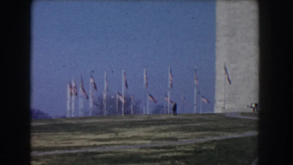 1960 Washington, DC frame showing flags around the Washington Monument and a lone distant person walking near the path.