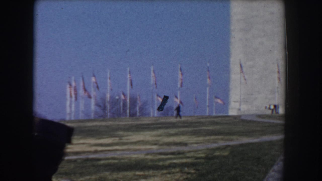 Washington Monument with flagpoles on the lawn and a small pedestrian nearby.