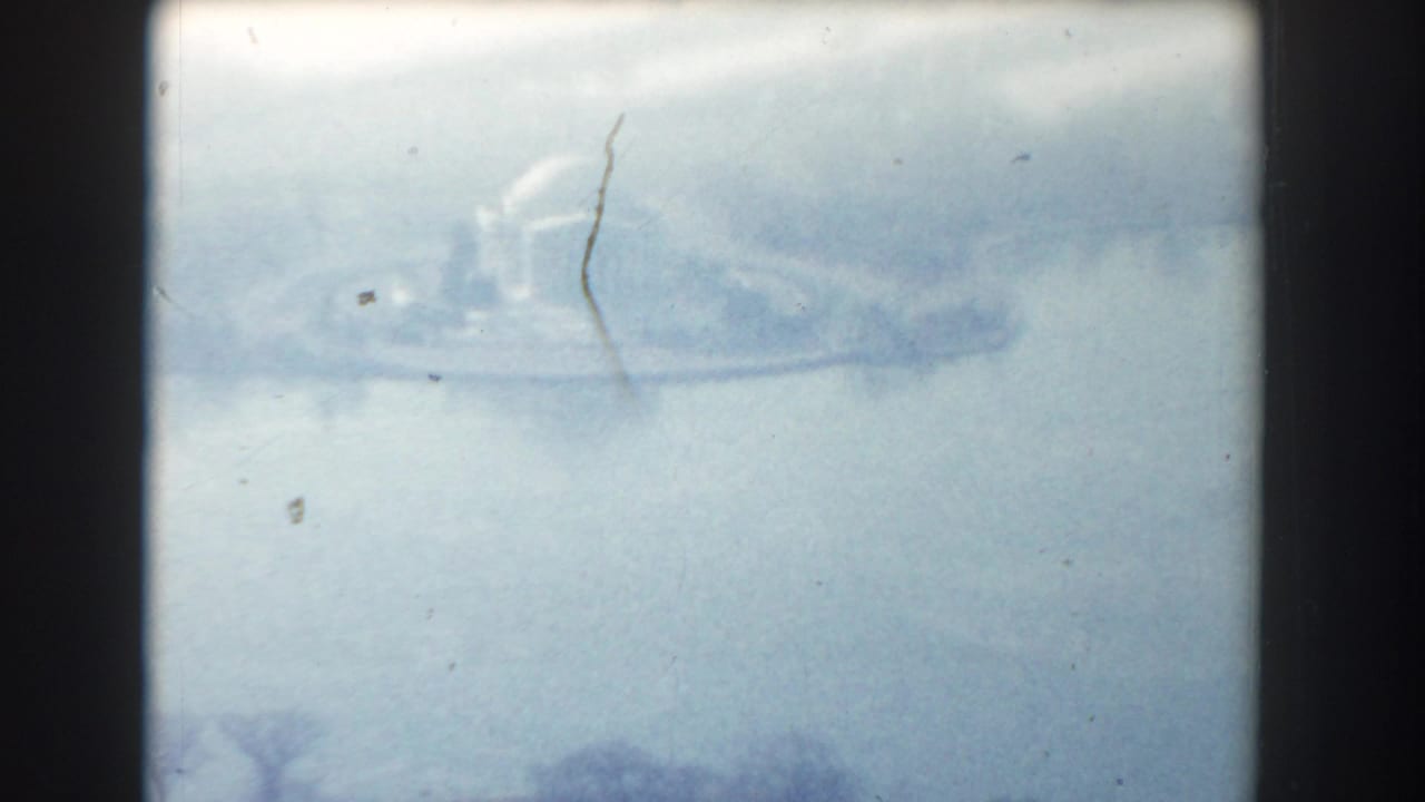 Soft aerial view of a domed memorial-like building across water, framed by dark film borders.
