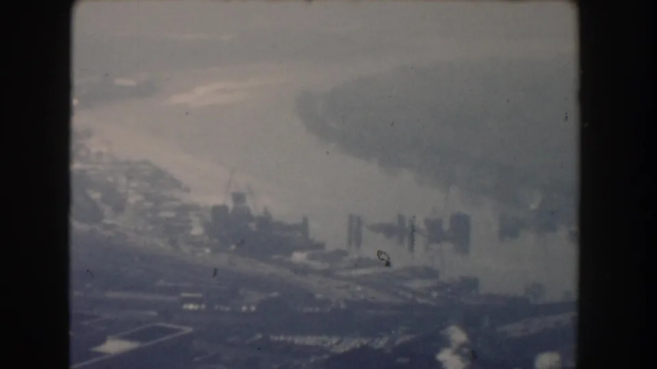 Broader 1960 Washington, DC aerial view over a riverfront cityscape with shoreline, piers or cranes, and wooded edges.