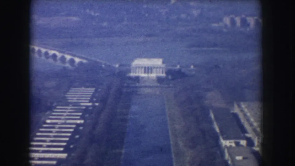 Blue-tinted 1960 8mm aerial view of the Lincoln Memorial area with the Reflecting Pool, bridge, roads, and surrounding trees.
