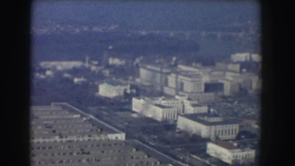 Soft 1960 Washington, DC aerial view showing large public buildings, roads, trees, and open grounds.