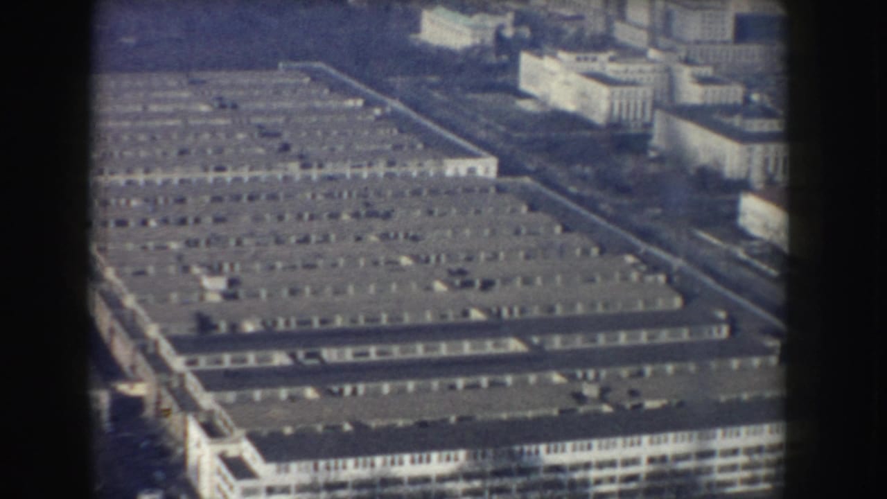 Aerial view over long city buildings with flat rooftops and surrounding downtown blocks.