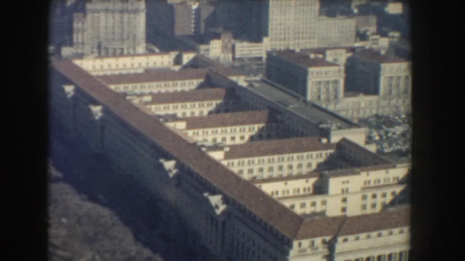 1960 Washington, DC aerial view of a long institutional-looking building with red-brown roofs and downtown towers beyond.