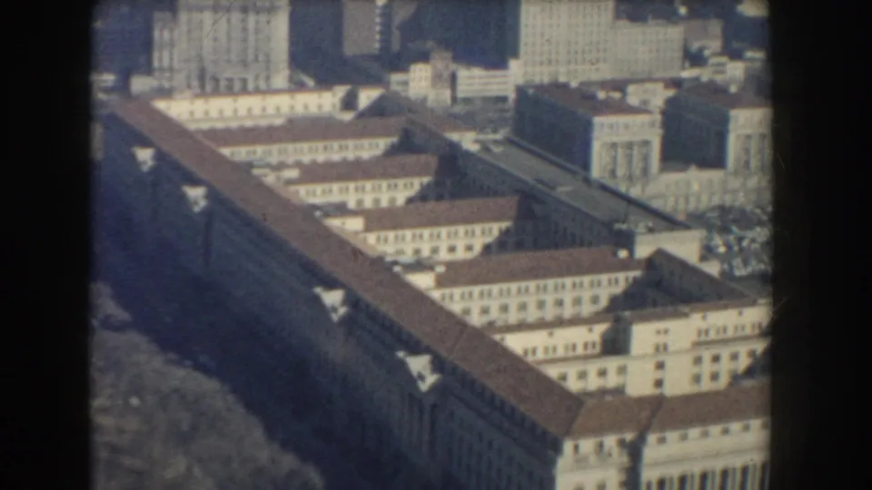 1960 Washington, DC aerial frame showing repeated roof sections on a large building complex with city high-rises in the background.